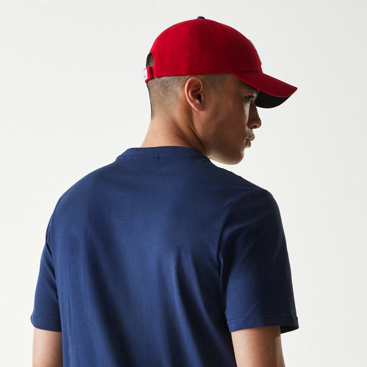 New Era Philadelphia Phillies MLB Regular Dark Blue T-Shirt, on-model view showing the back of a person wearing a dark blue T-shirt paired with a red cap, the cap featuring a debossed logo on the back strap.