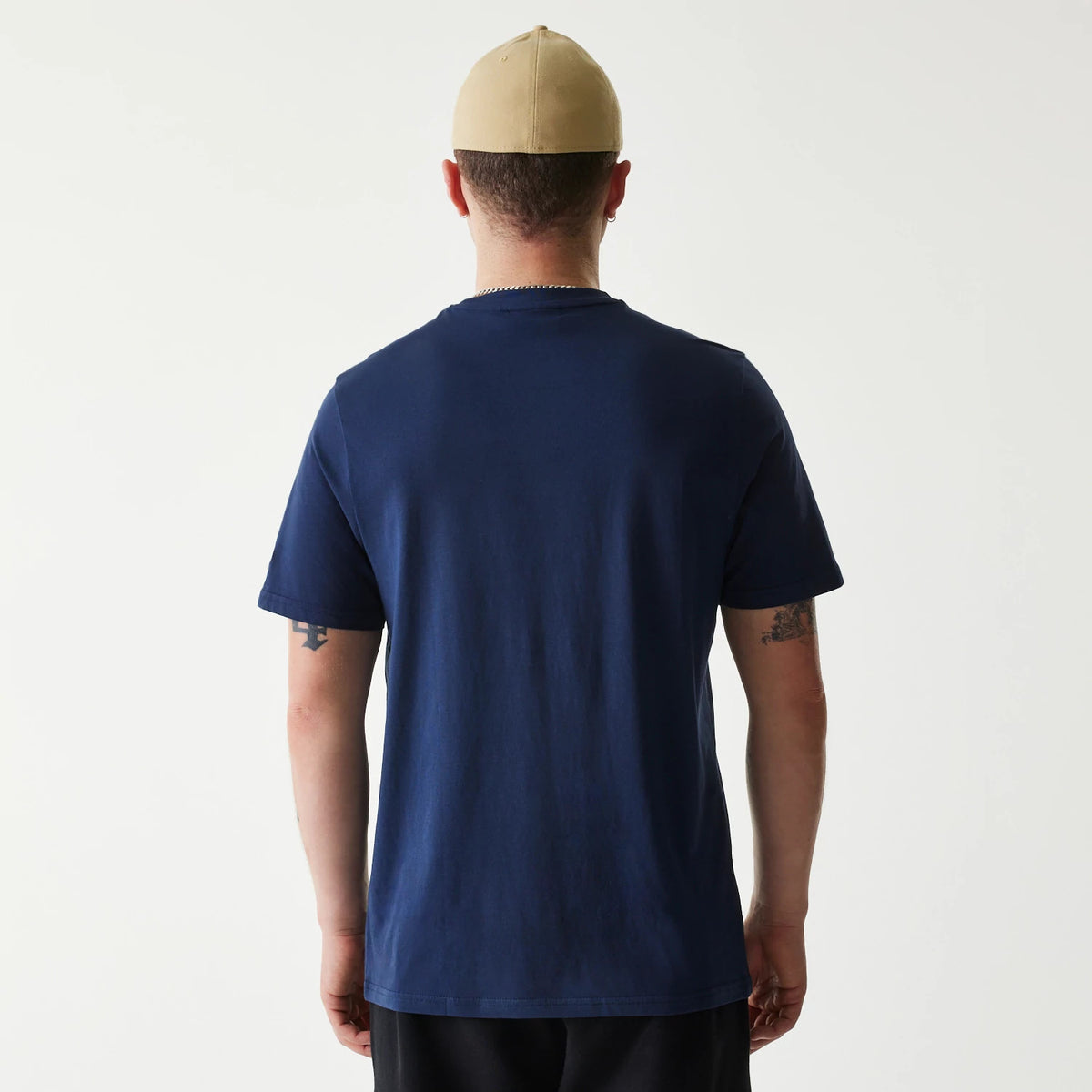 New Era Milwaukee Brewers MLB Regular Dark Blue T-Shirt, rear view showing the plain dark blue back and short sleeves worn by a person with a beige cap, exposing only their arms and neck.