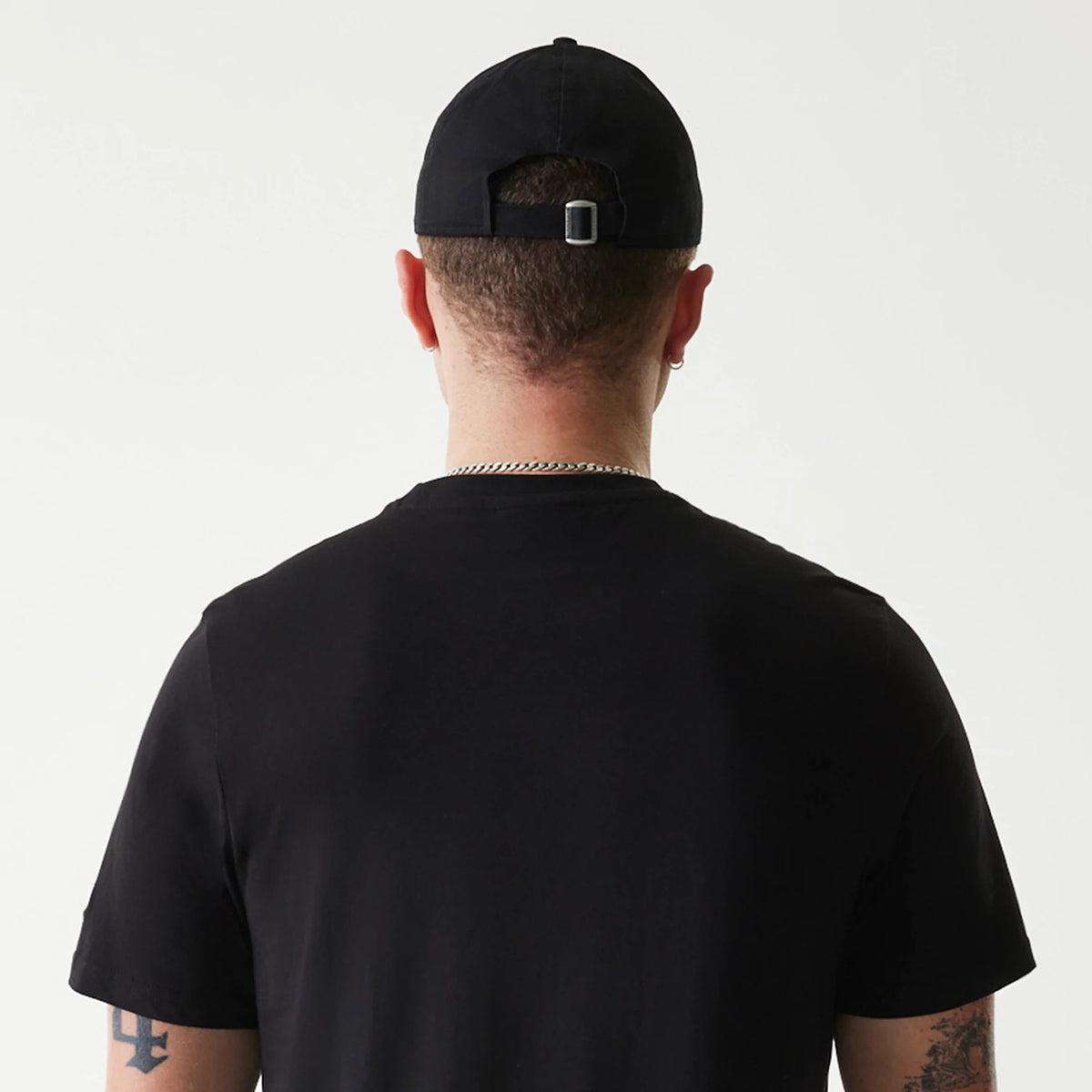 New Era Pittsburgh Pirates MLB Regular Black T-Shirt, rear view showing the plain black fabric across the back and shoulders worn beneath a black cap with an adjustable strap and buckle at the back of the head.
