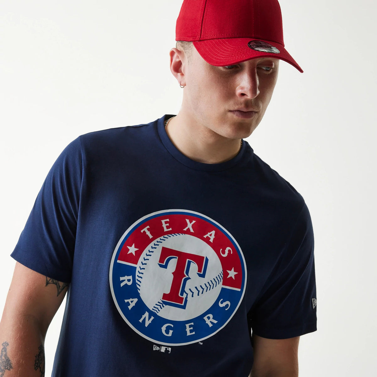 New Era Texas Rangers MLB Regular Dark Blue T-Shirt, on-model view displaying the circular Texas Rangers logo with a baseball motif centred on the chest in red, white and blue, paired with a red cap featuring a raised New Era logo on the front.