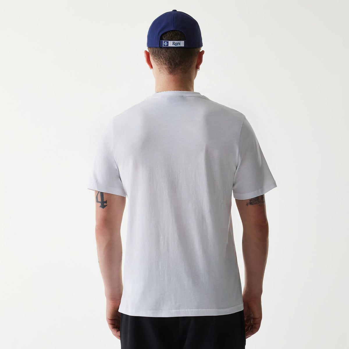 New Era Tampa Bay Rays MLB Regular White T-Shirt, on-model rear view showing the plain white back design, straight hem, and relaxed short sleeves, paired with a blue cap featuring a raised Rays logo at the back.