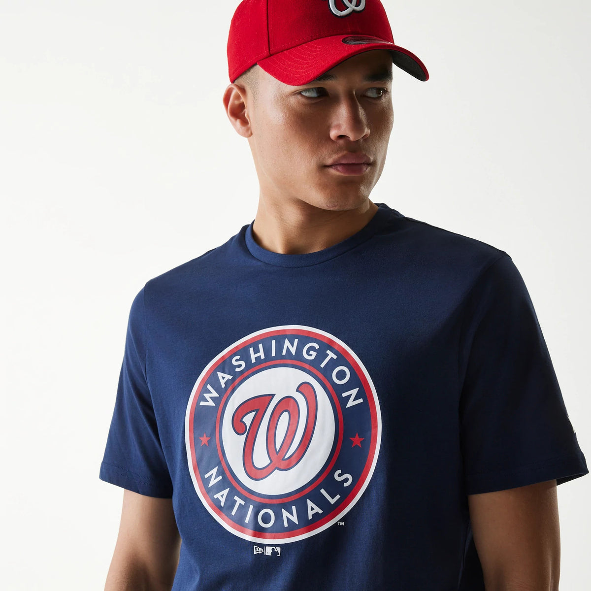 New Era Washington Nationals MLB Regular Dark Blue T-Shirt, three-quarter view showcasing the large printed team logo in red and white on the chest, worn by a person also wearing a red cap with a raised team logo at the front.