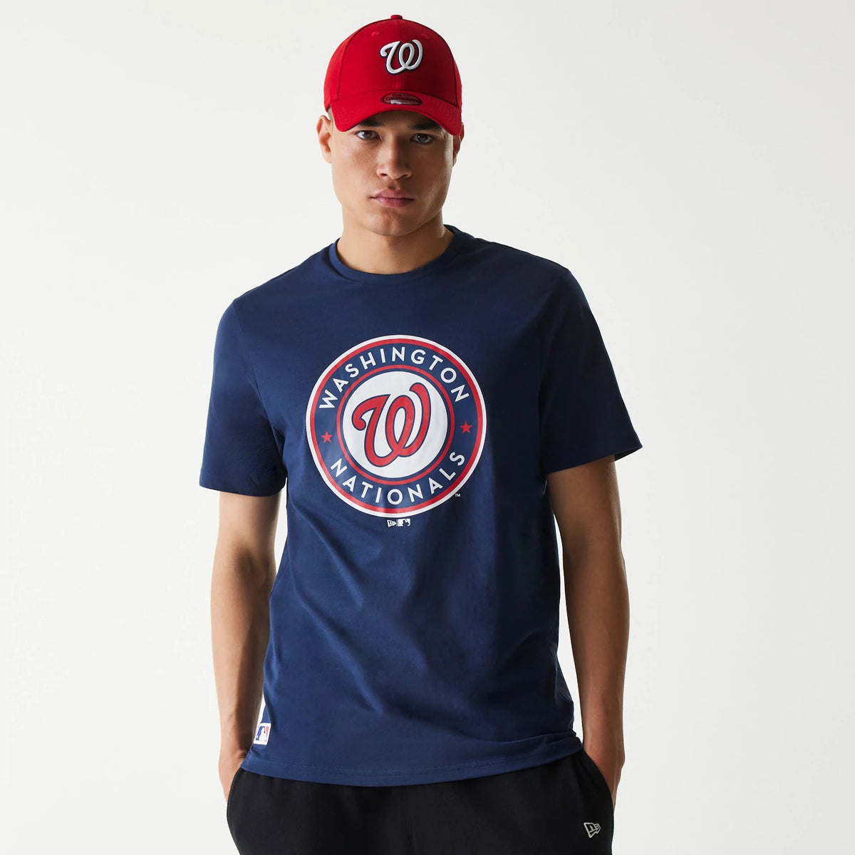 New Era Washington Nationals MLB Regular Dark Blue T-Shirt, front view showing the large circular Washington Nationals logo with red accents centred on the chest, worn by a model wearing a red cap with an embossed 'W' logo.
