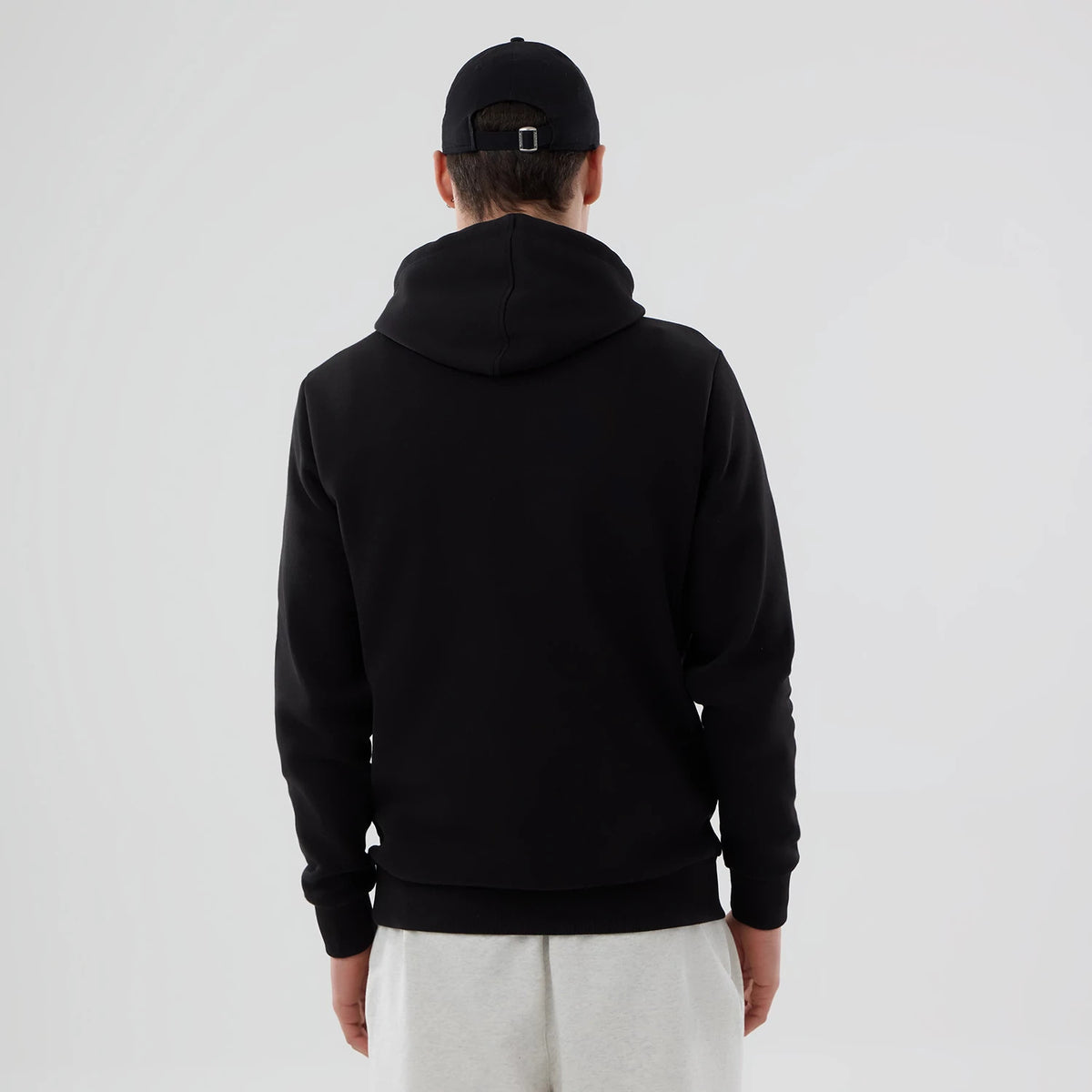New Era Cincinnati Reds MLB Black Pullover Hoodie, rear view showing the plain black fabric with a large hood, worn by a person also dressed in a black cap and light grey trousers, no logo or additional features visible on the back.