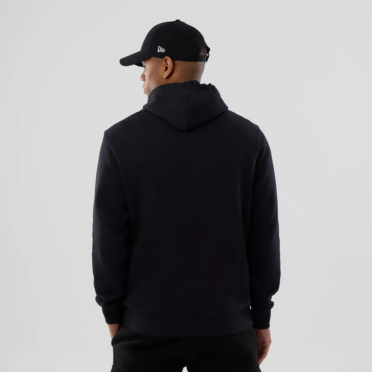 New Era Cleveland Guardians MLB Navy Pullover Hoodie, rear view showing the plain navy back with a relaxed hood and long sleeves, worn by a person also in a black cap with an embossed logo on the side.