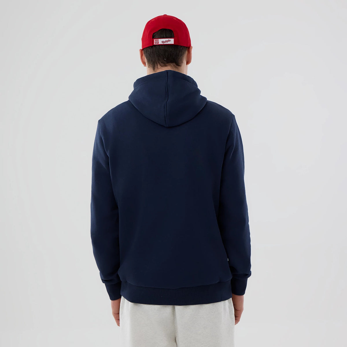 New Era Washington Nationals MLB Dark Blue Pullover Hoodie, rear view showing the dark blue hoodie with a simple design, worn by a person also wearing a red cap, the hood resting flat against the back.
