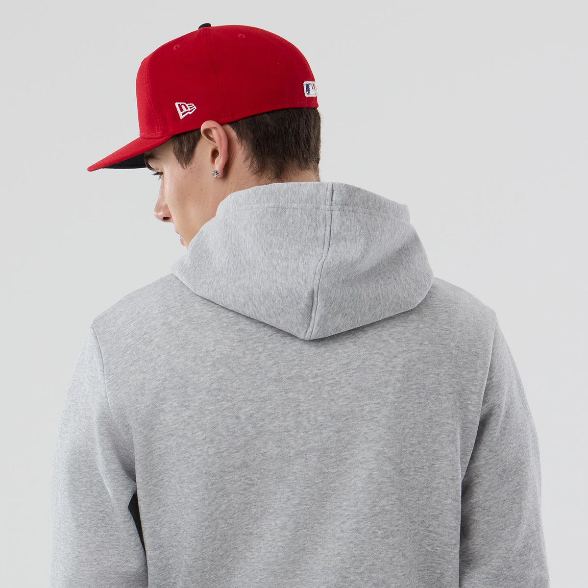 New Era Philadelphia Phillies MLB Grey Pullover Hoodie, rear view showing the plain grey hood covering the upper back, with a red cap featuring a raised New Era logo on the side worn by the model.