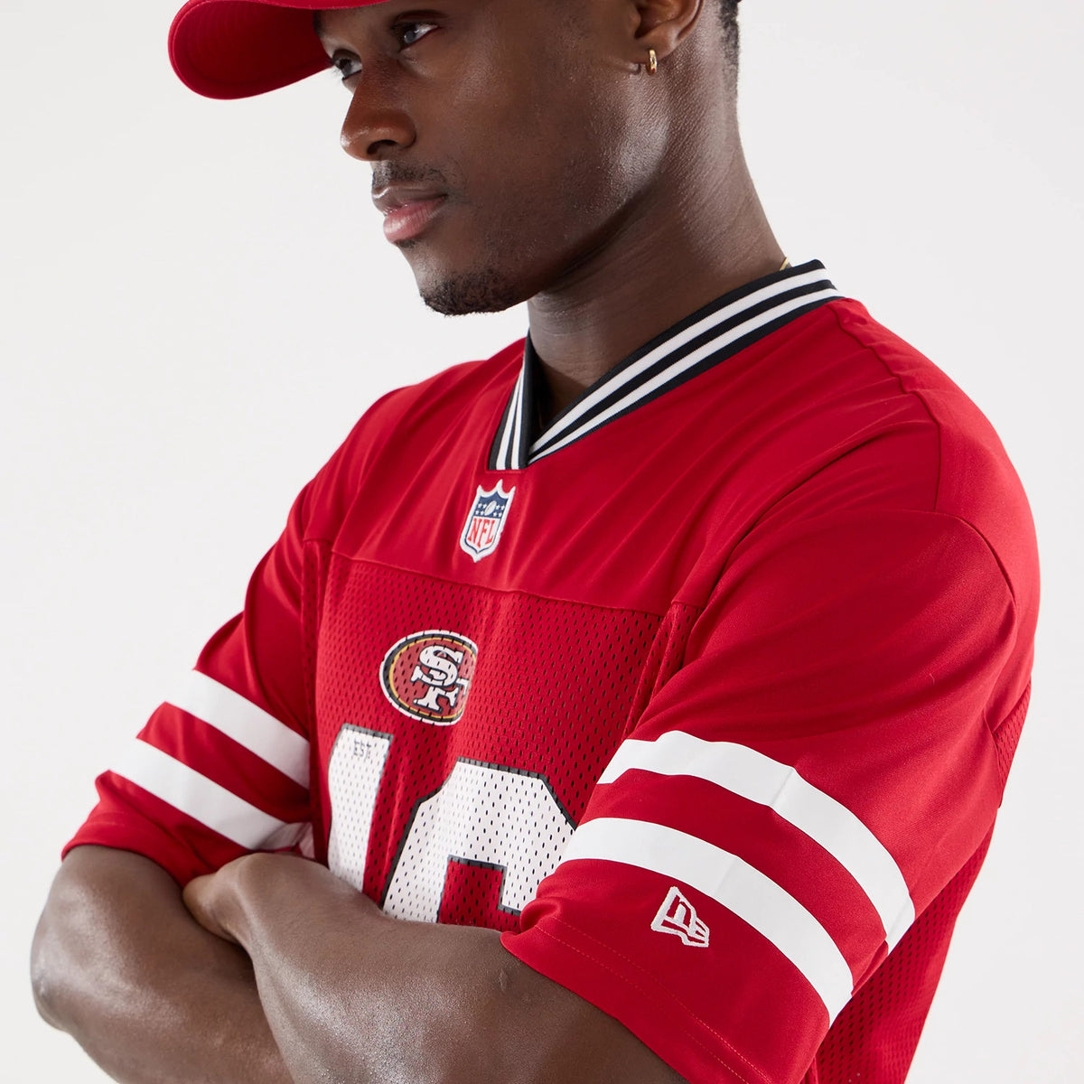 New Era San Francisco 49ers NFL Mesh Red Mesh Jersey, side view on a model with a matching red cap, showing the embroidered 49ers logo on the chest and the New Era flag logo on the left sleeve above white stripe details.