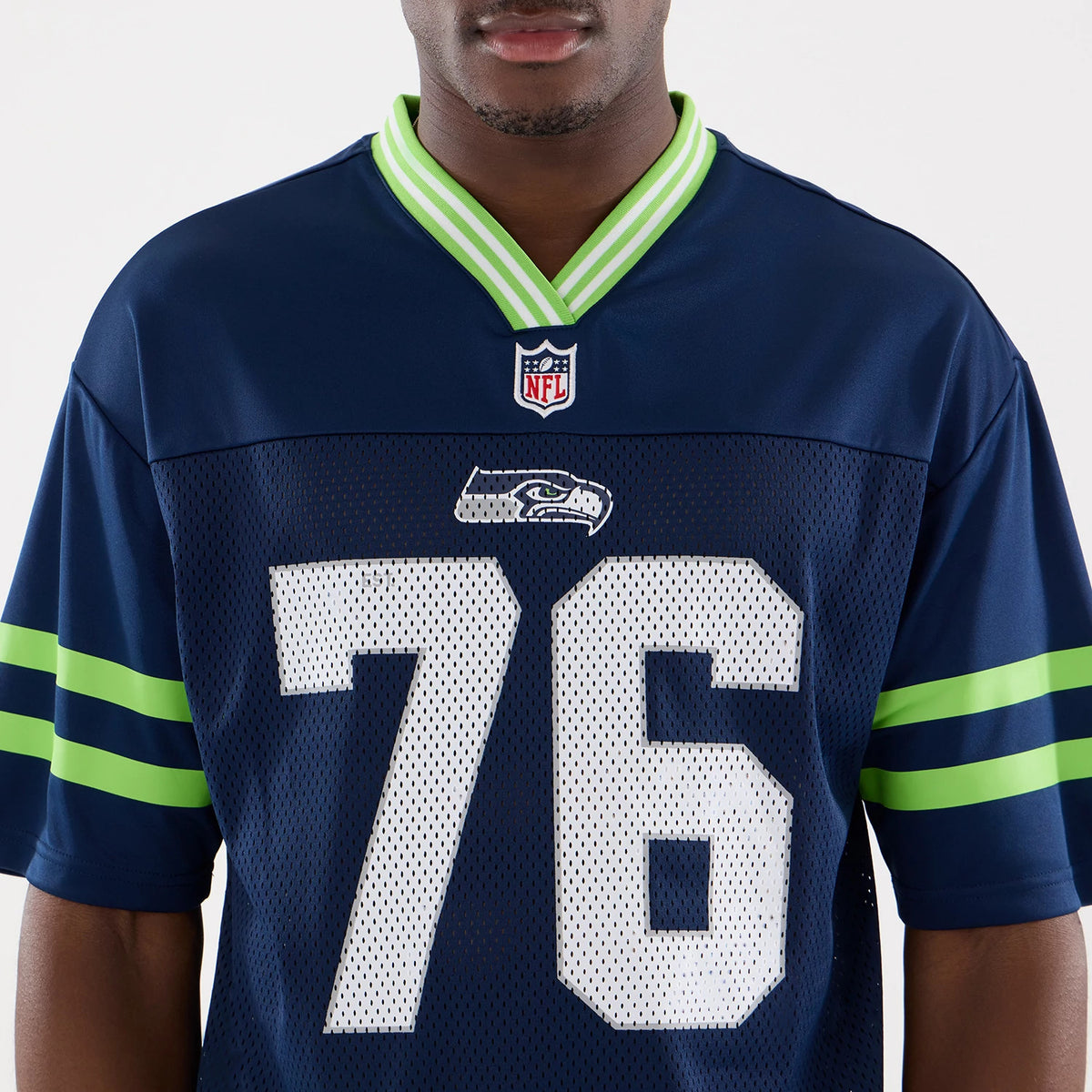 New Era Seattle Seahawks NFL Mesh Dark Blue Mesh Jersey, front view on a model showing the large white number 76, the embroidered team logo beneath the NFL shield on the chest, and the green and blue stripes on the sleeves.