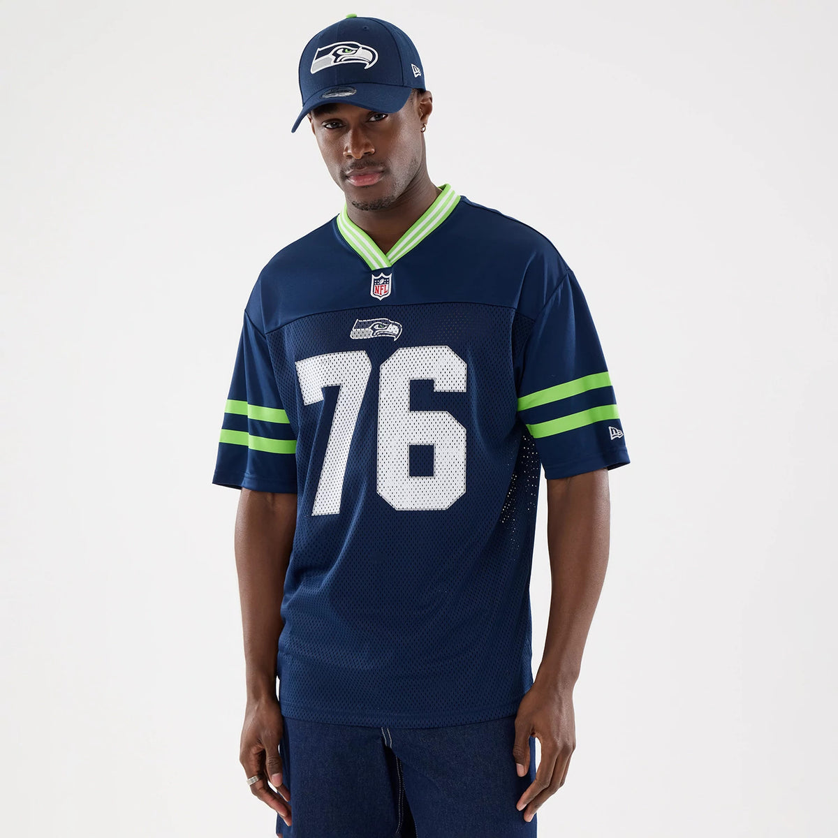 New Era Seattle Seahawks NFL Mesh Dark Blue Mesh Jersey, front view on a model styled with a matching cap, featuring the number 76 in white centred on the chest, green stripes on the sleeves, and a V-shaped collar.