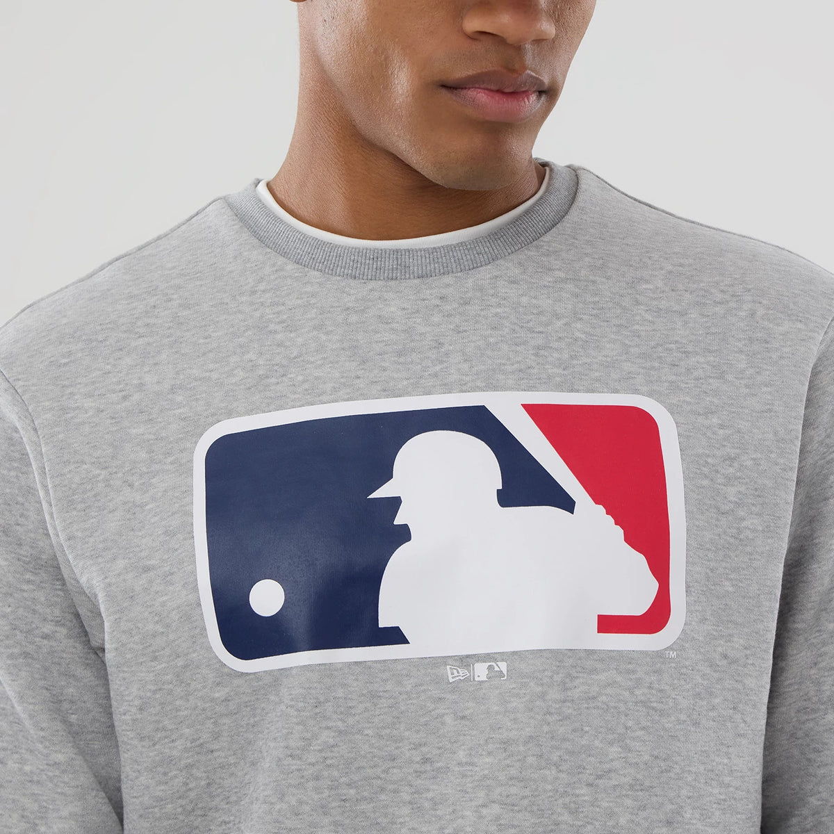 New Era MLB Generic Logo Grey Crew Neck Sweater, front view on a model showing the large MLB logo centred on the chest with red, white, and blue elements, highlighting the classic grey ribbed crew neck.