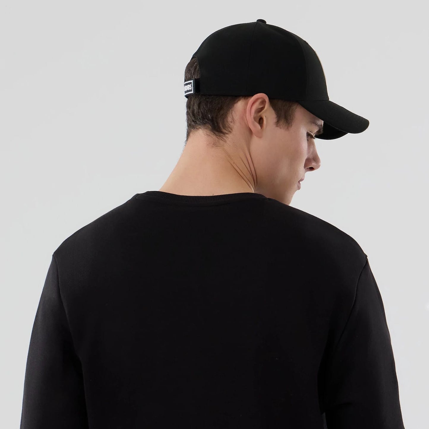 New Era Las Vegas Raiders NFL Core Black Crew Neck Sweater, on a model with a black cap showing embroidered Raiders lettering on the centre back, highlighting the sweater's relaxed fit and crew neck design.