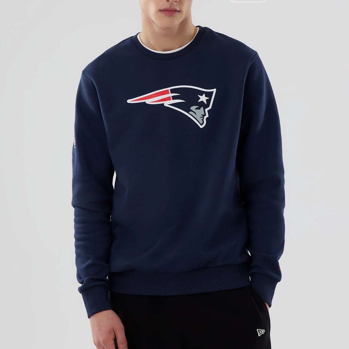 New Era New England Patriots NFL Dark Blue Crew Neck Sweater, front view on a model wearing black trousers, displaying a large Patriots logo across the chest and a New Era flag logo on the left sleeve.