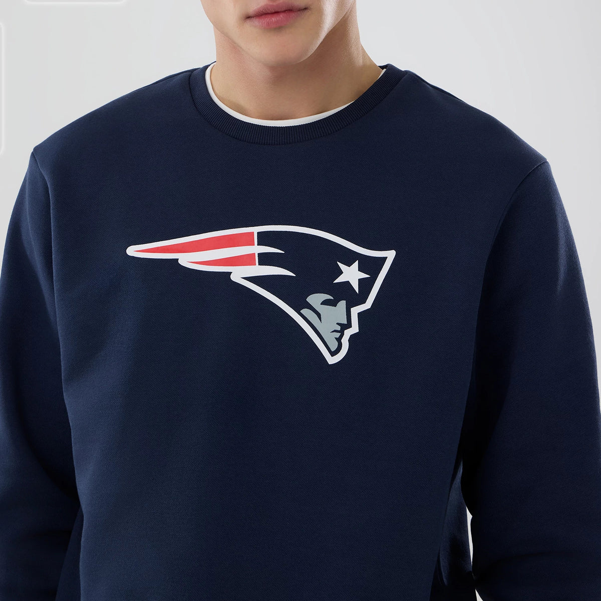New Era New England Patriots NFL Dark Blue Crew Neck Sweater, front view on a model showing the large team logo in red, white, and blue printed across the chest, with a ribbed collar and dark blue fabric.