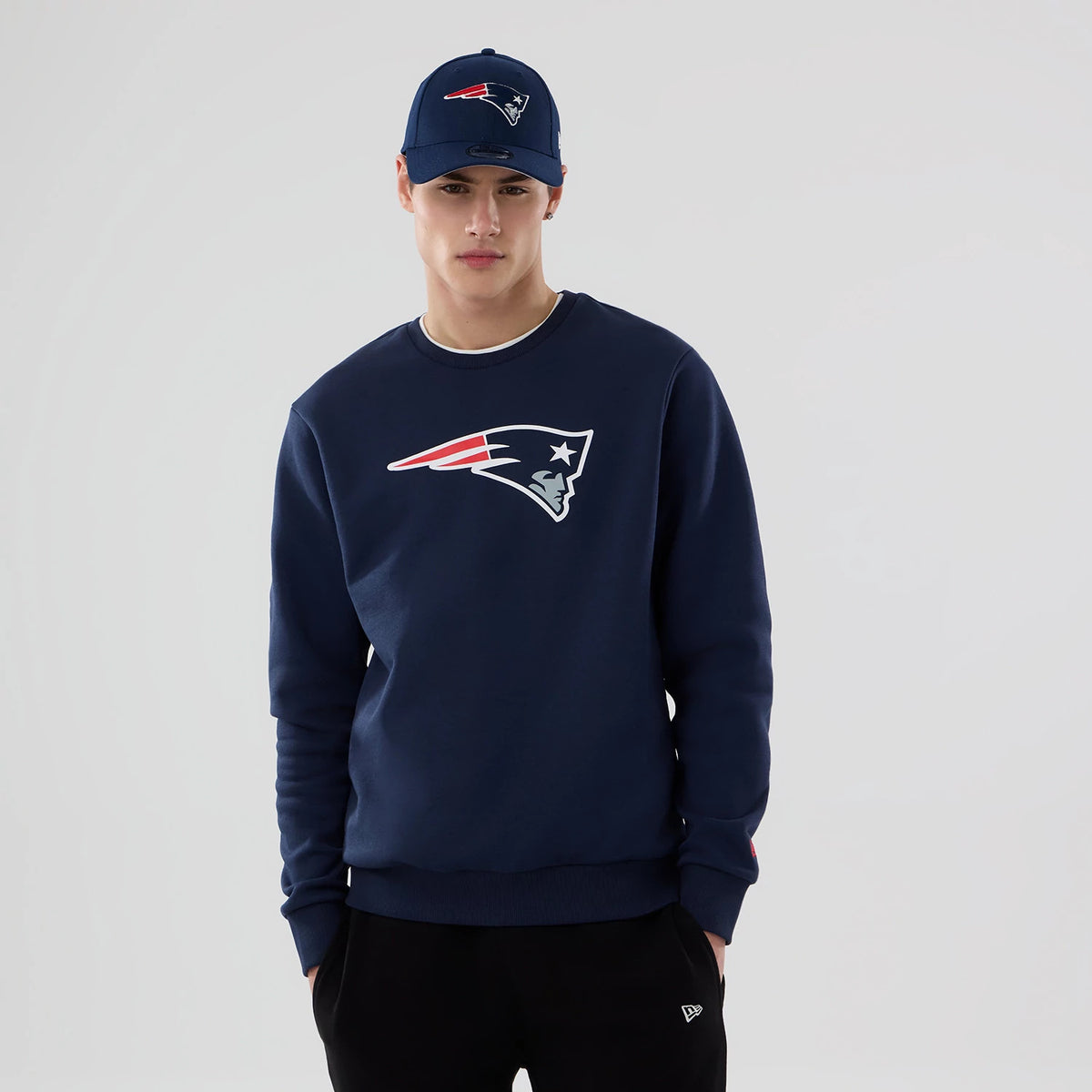 New Era New England Patriots NFL Dark Blue Crew Neck Sweater, front view on a model wearing a matching cap, featuring the team logo centred on the chest, with ribbed cuffs and hem.