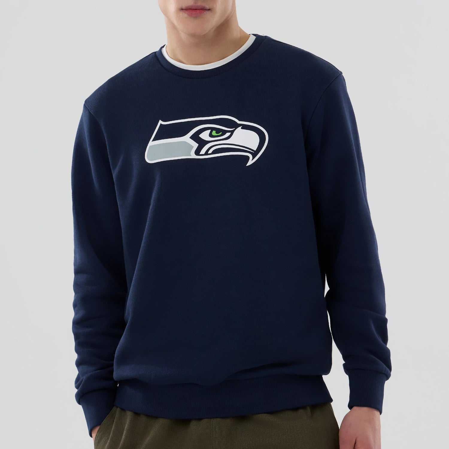 New Era Seattle Seahawks NFL Dark Blue Crew Neck Sweater, front view on a model wearing olive trousers, with a large embroidered white, grey, and green Seahawks logo centred on the chest.
