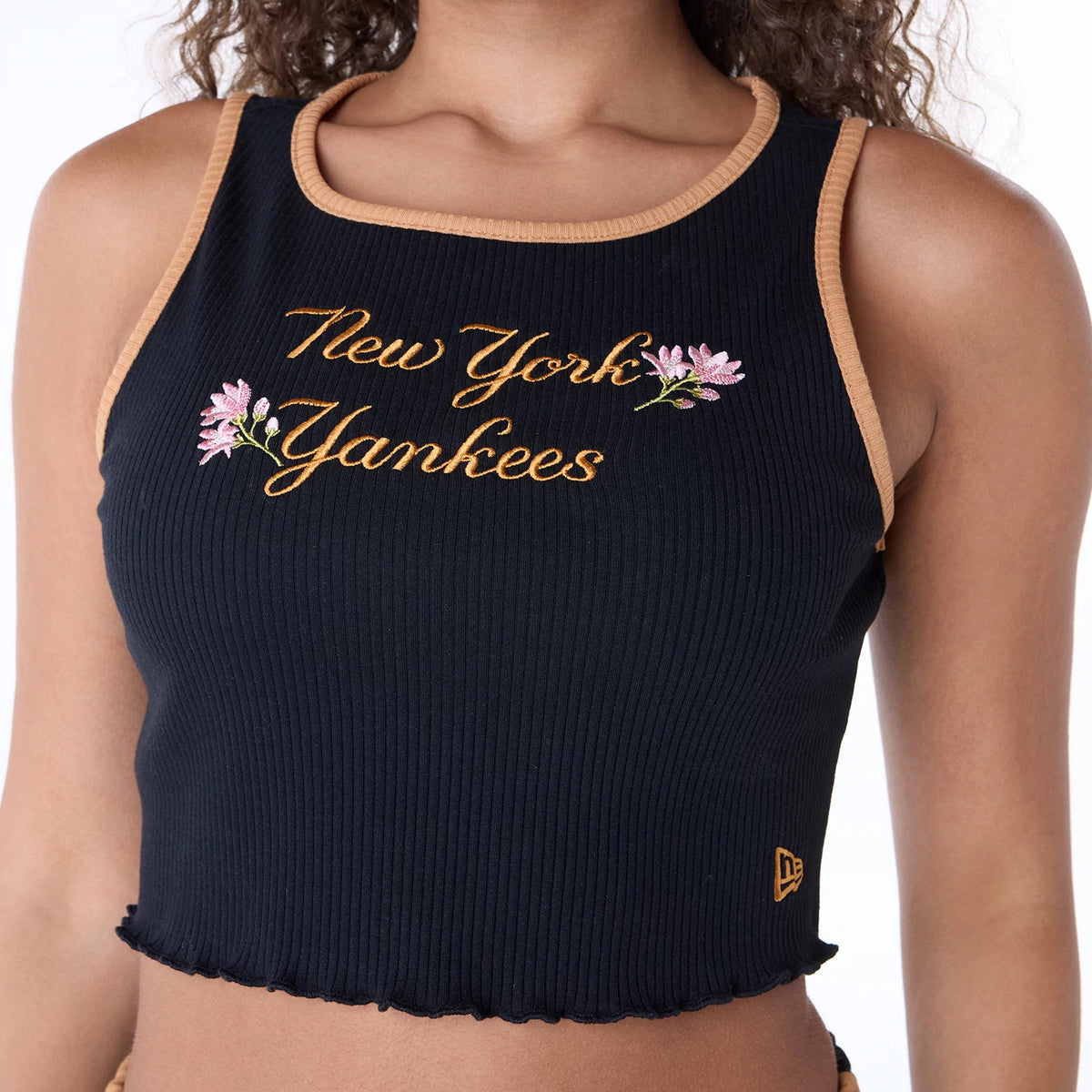 New Era New York Yankees Womens MLB Floral Black Vest, front view on a model with orange embroidered lettering and pink flowers across the chest, featuring ribbed texture and orange piping around the armholes and neckline.