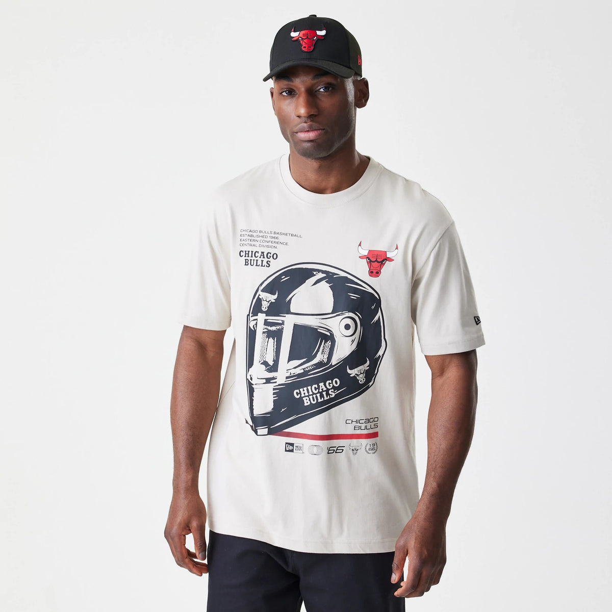 New Era Chicago Bulls Modern Driver Light Beige T-Shirt, on-model view showing a large graphic of a black helmet with text on the front, a red debossed Chicago Bulls logo above and a small New Era logo on the left sleeve.