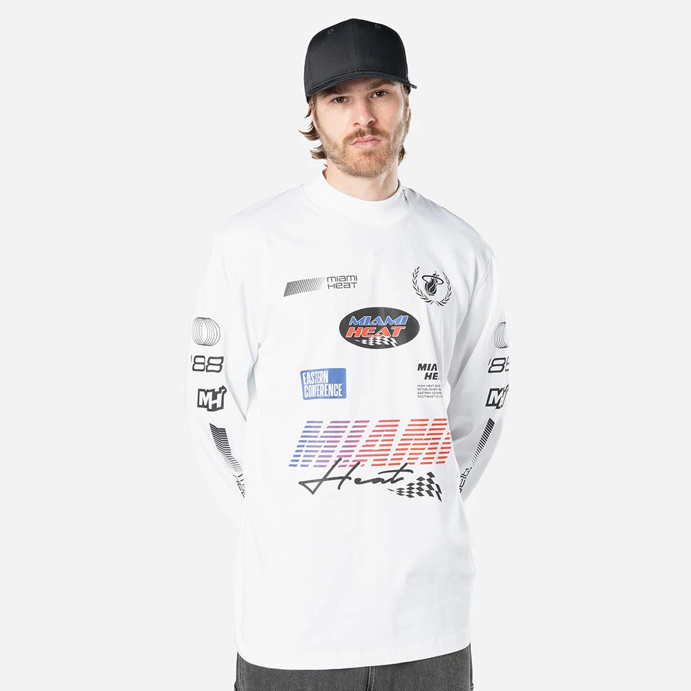 New Era Miami Heat Modern Driver White Long Sleeve T-Shirt, front view showing a variety of logos and designs in black, blue, red, and orange on the chest and sleeves, worn by a person with a black cap.