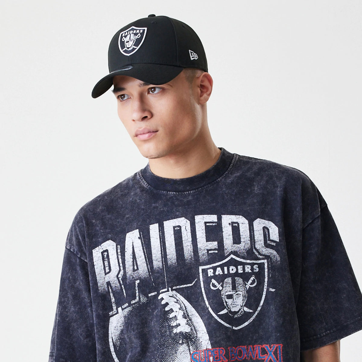 New Era Las Vegas Raiders Sport Classic Black T-Shirt, on-model view showing a distressed black t-shirt with a large white Raiders logo and text on the chest, accompanied by a black cap featuring an embossed New Era logo on the side.