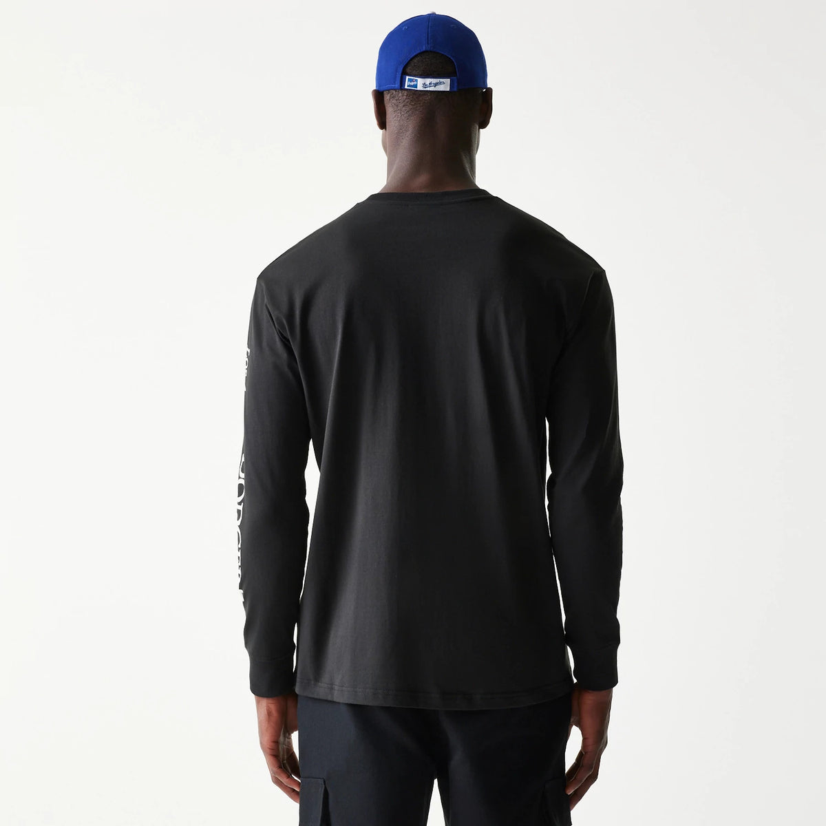 New Era LA Dodgers MLB Character Black Long Sleeve T-Shirt, rear view showing a plain back with white printed graphics down the right sleeve and a blue cap worn backwards with a raised logo on the cap's strap above the neck.
