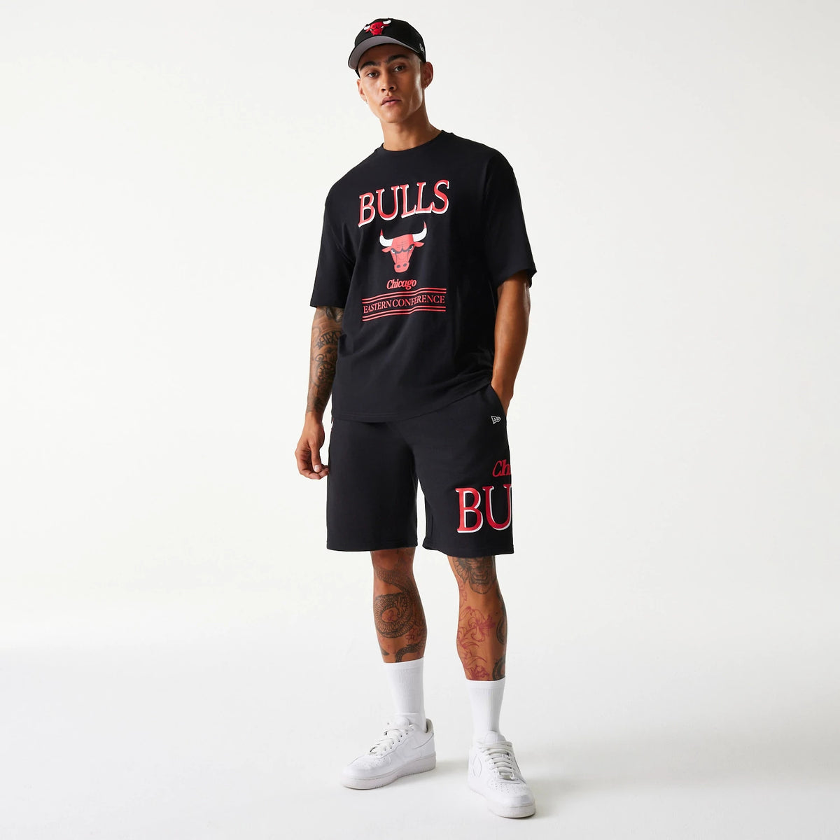 New Era Chicago Bulls NBA Team Graphic Black Oversized T-Shirt, on-model view showing the black t-shirt with bold red Bulls logo on the chest and a matching black cap with a raised Bulls logo on the front crown.