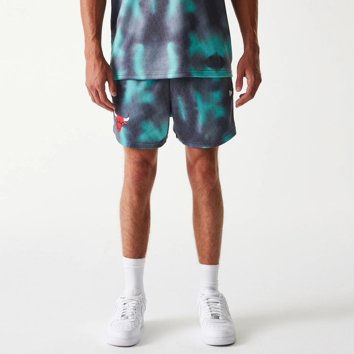 New Era Chicago Bulls NBA All Over Print Green Shorts, front view showing a multicoloured pattern with the red embroidered Chicago Bulls logo on the left leg and a debossed New Era logo on the right side.
