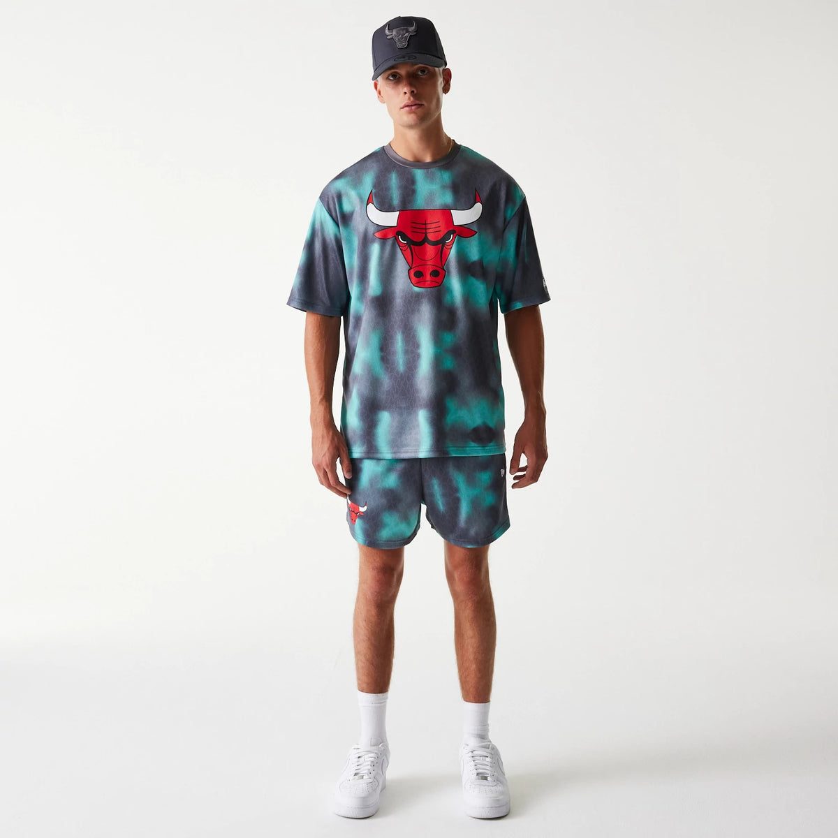 New Era Chicago Bulls NBA All Over Print Green Shorts, on-model view showing the shorts with a red Chicago Bulls logo on the left thigh, part of a coordinated set with a matching top displaying a large front logo.