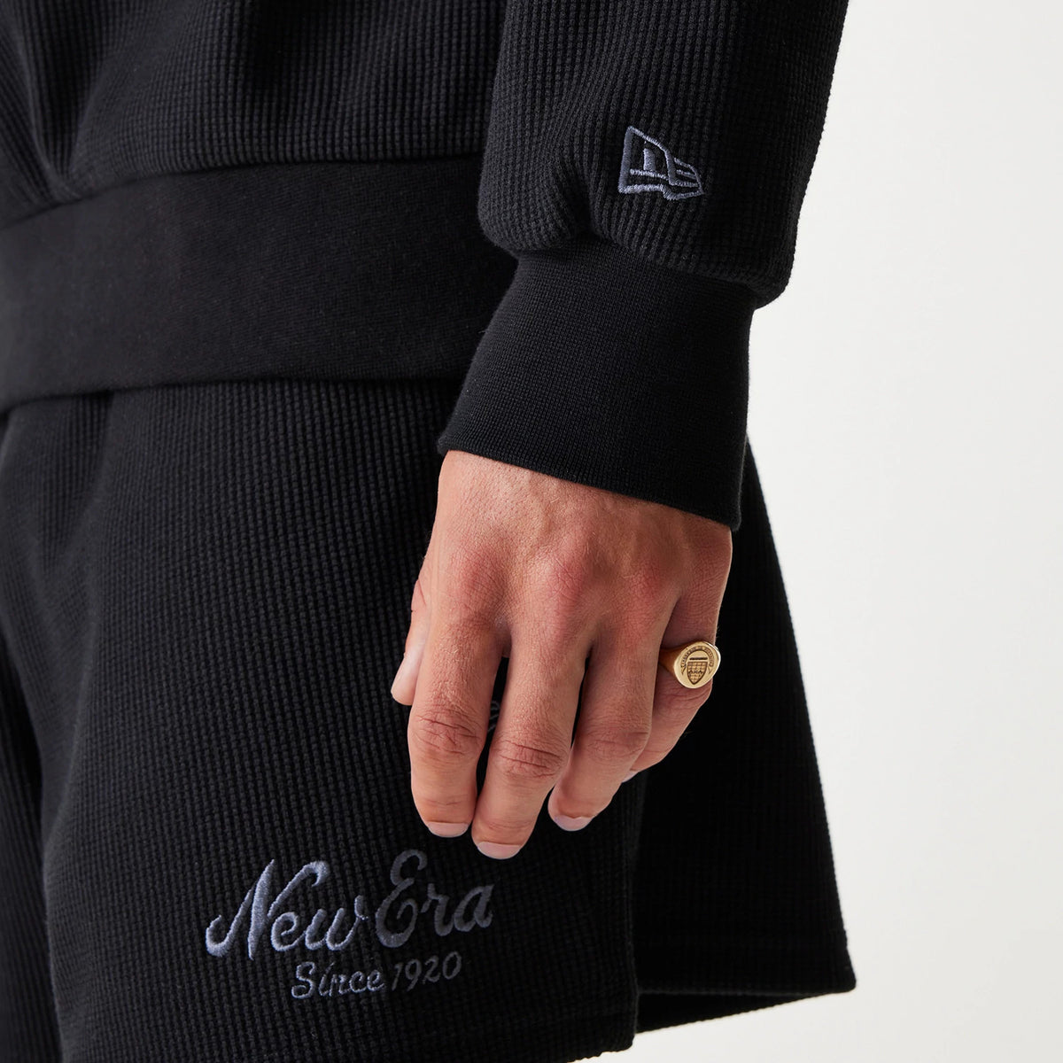 New Era Waffle Black Oversized Crew Neck Sweater, close-up showing the textured waffle knit fabric with the New Era flag logo on the cuff, paired with matching shorts featuring New Era Since 1920 embroidery above the hem.