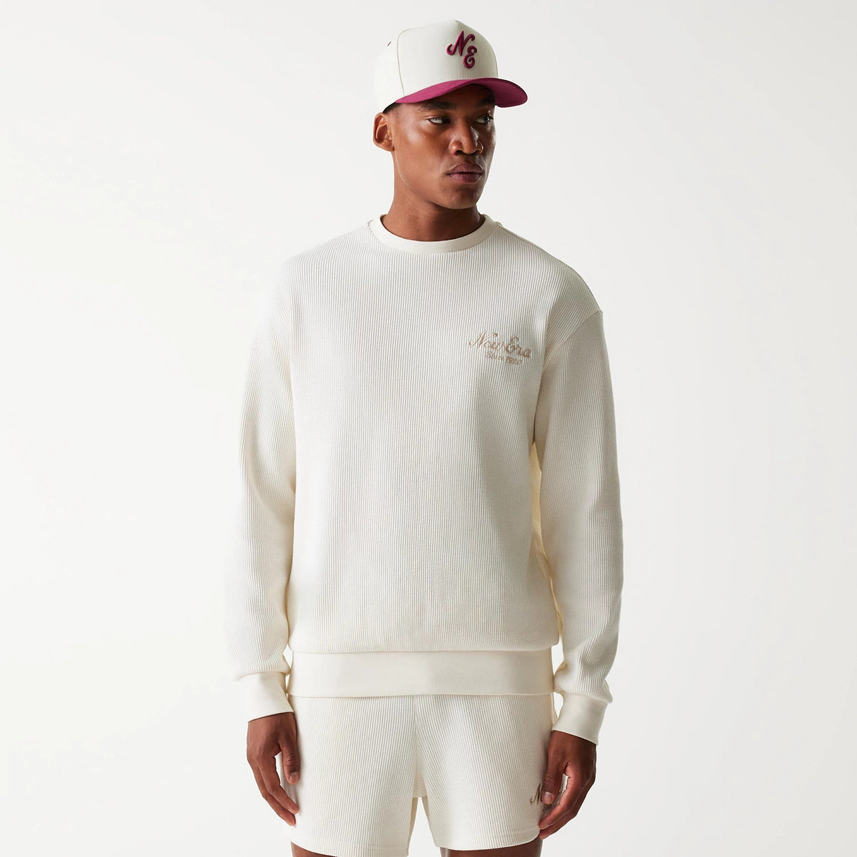 New Era Waffle Open White Oversized Crew Neck Sweater, on-model view styled with a white and burgundy cap, showing an embroidered logo on the left chest and ribbed texture throughout the body and sleeves.