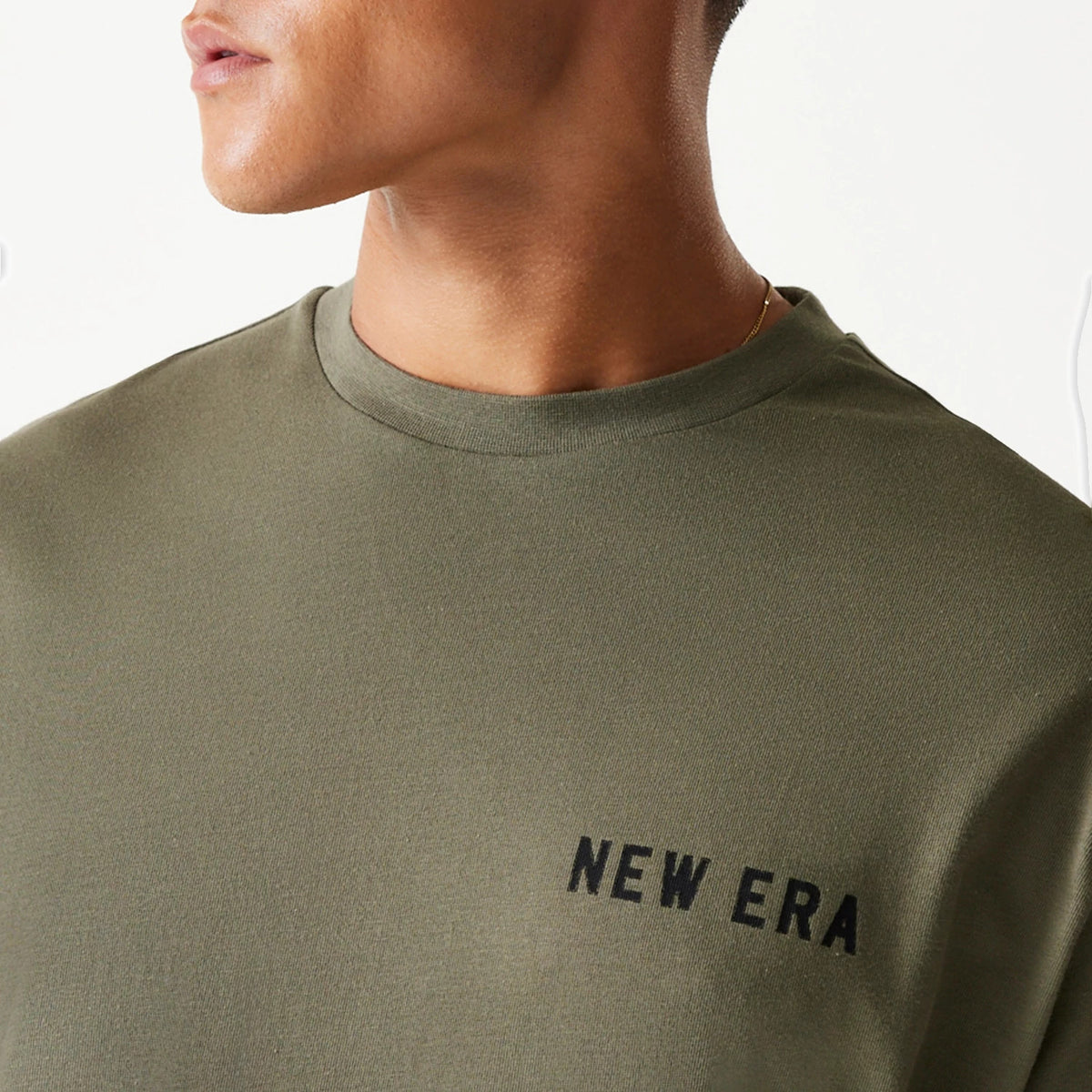 New Era Animal Graphic Green Oversized T-Shirt, on-model view showing the olive green fabric and a black raised New Era logo on the left chest, with a close-up of the crew neckline.