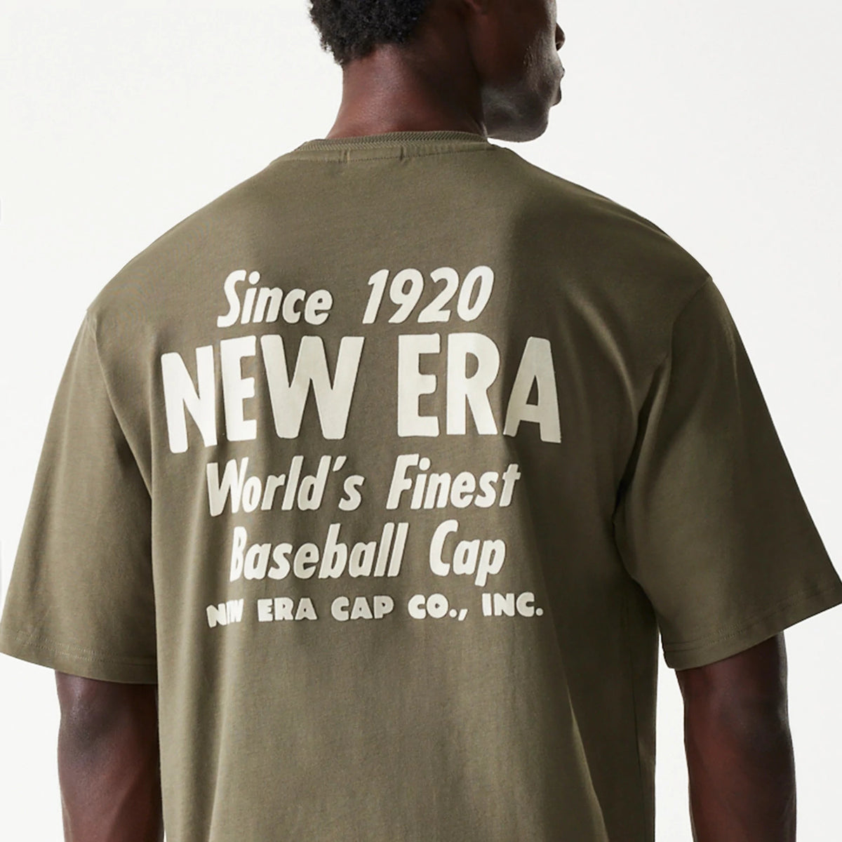 New Era Graphic Green Oversized T-Shirt, rear view showing large white printed text Since 1920 NEW ERA World's Finest Baseball Cap across the upper back of the green fabric, highlighting the casual style of the garment.