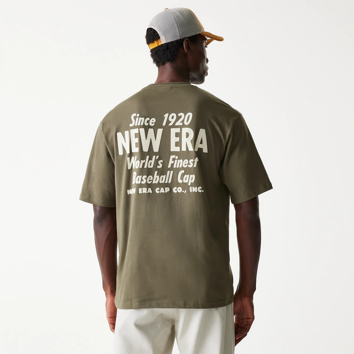 New Era Graphic Green Oversized T-Shirt, on-model view showing the back of the garment with large white graphic text including NEW ERA and World's Finest Baseball Cap across the shoulders on a green background.