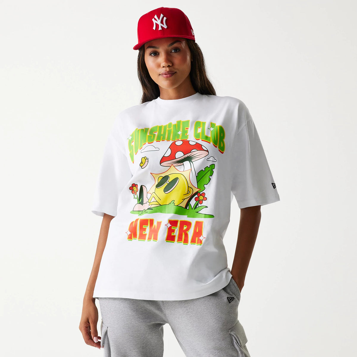 New Era Outdoor Graphic White Oversized T-Shirt, on-model view showing a colourful graphic with a sun wearing sunglasses and a mushroom, the words Sunshine Club in green and New Era in red across the front.