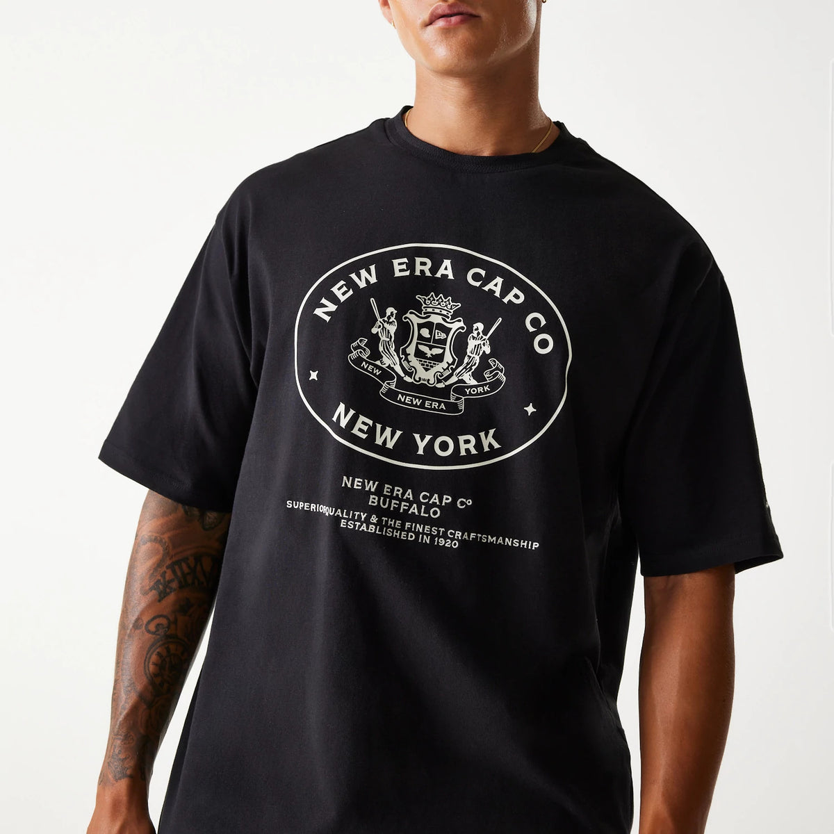 New Era Crest Black Oversized T-Shirt, front view showing the large white printed emblem centred on the chest, featuring the New Era crest and text below reading New Era Cap Co Buffalo on a loose-fitting black shirt.