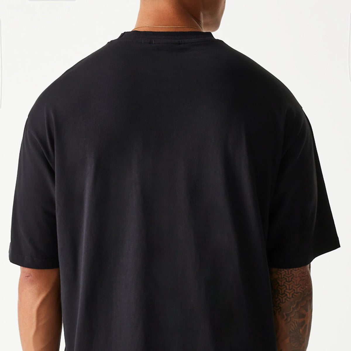 New Era Crest Black Oversized T-Shirt, rear view showing the plain black back and sleeves of the oversized design, with a close fit around the neck and short sleeves extending to the elbows.