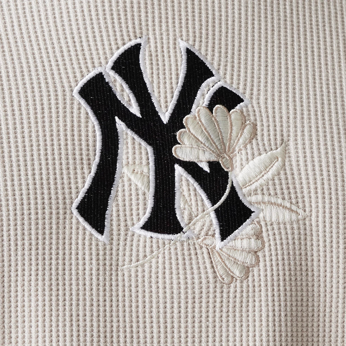 New Era New York Yankees MLB Waffle Cream Oversized Crew Neck Sweater, close-up showing the black NY logo embroidered on the textured cream fabric, accented with white floral designs intertwined with the logo.