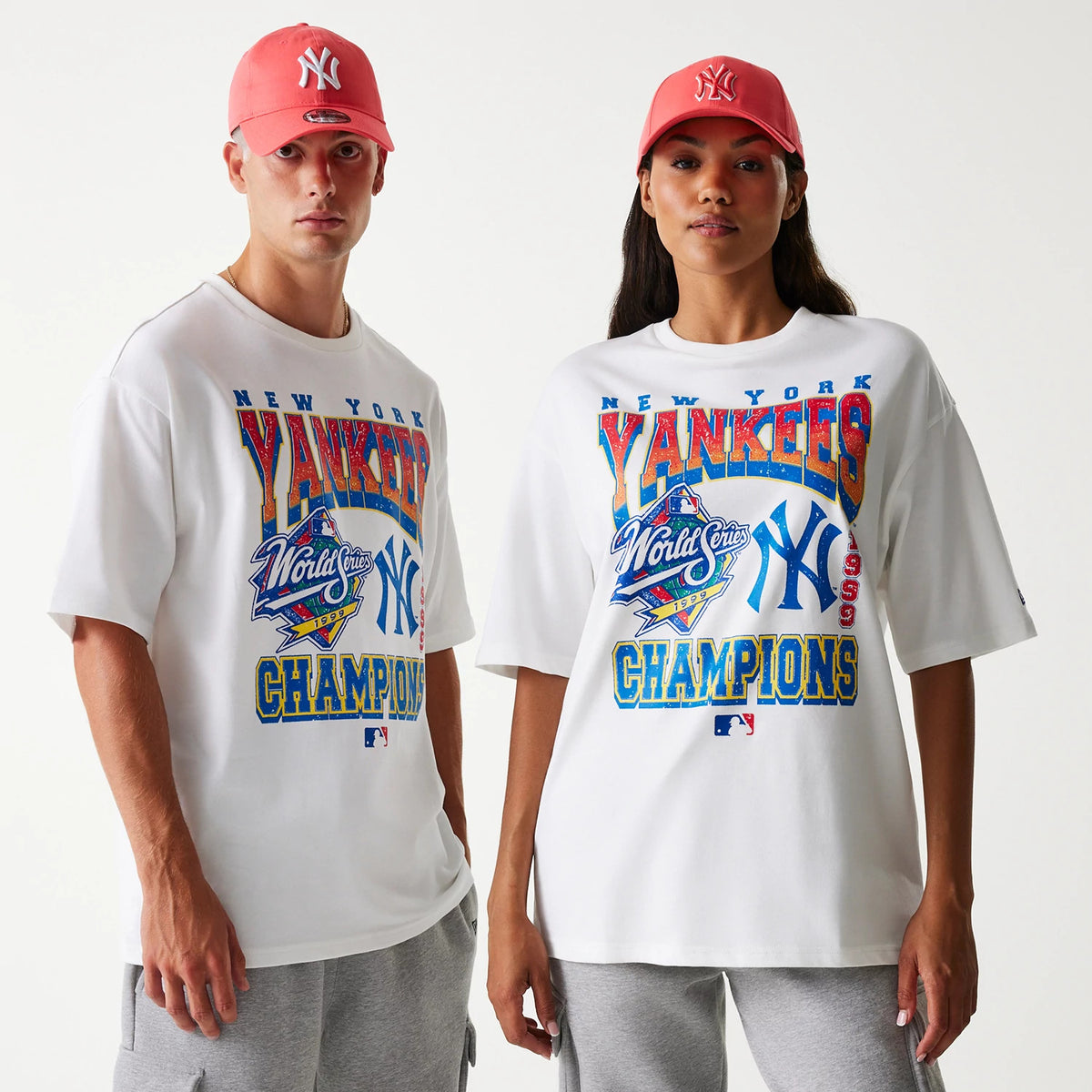 New Era New York Yankees MLB World Series 1999 White Oversized T-Shirt, front view showing large colourful graphics with the Yankees logo and World Series emblem printed on a white shirt worn by individuals in red caps.