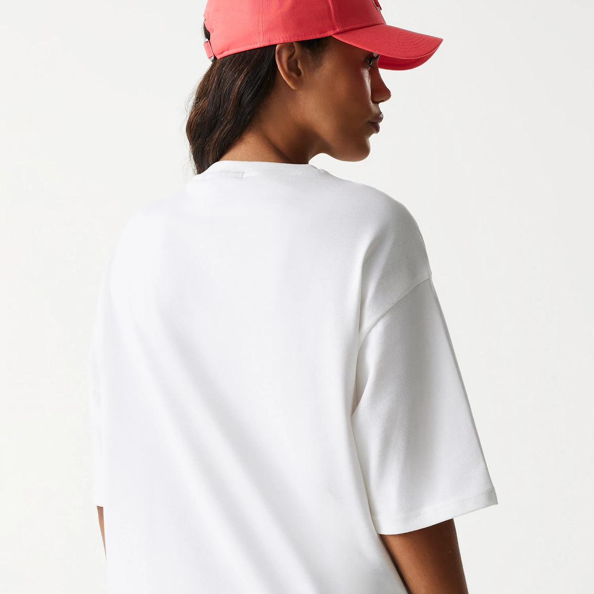 New Era New York Yankees MLB World Series 1999 White Oversized T-Shirt, on-model view showing the plain back of the oversized white T-shirt and a red cap with a raised logo worn by the model, side profile.