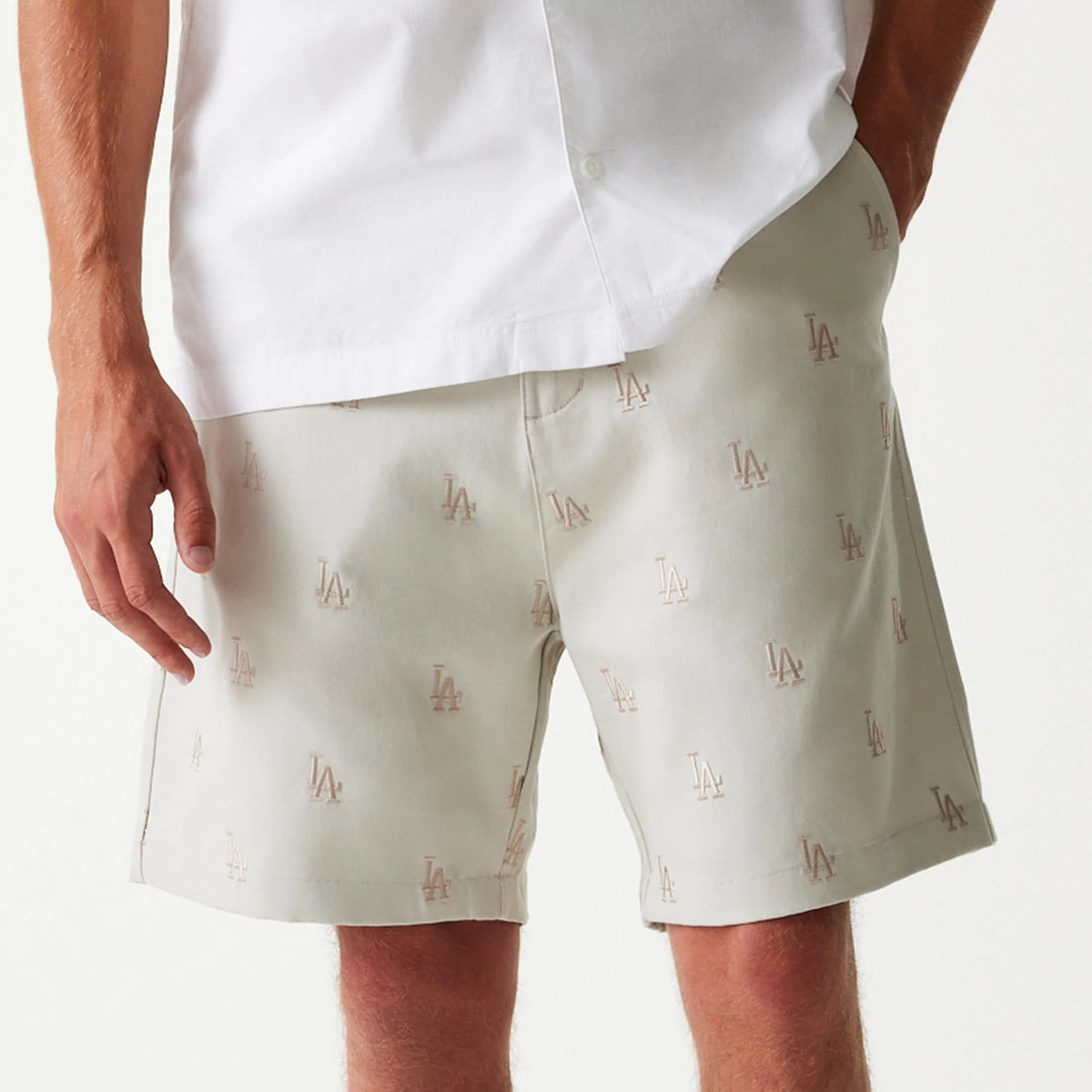 New Era LA Dodgers MLB Monogram Cream Shorts, front view showing cream shorts with an all-over debossed LA monogram, knee-length design and a straight hem paired with a white shirt.