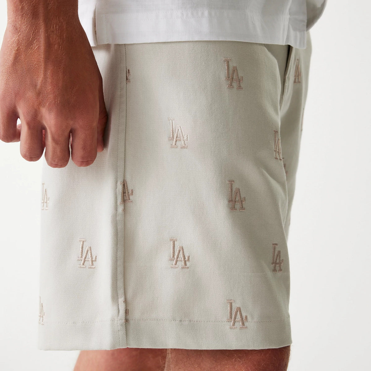 New Era LA Dodgers MLB Monogram Cream Shorts, side view showing cream-coloured shorts with an embroidered LA logo pattern throughout, the hem just above the knee, and a subtle seam along the side.