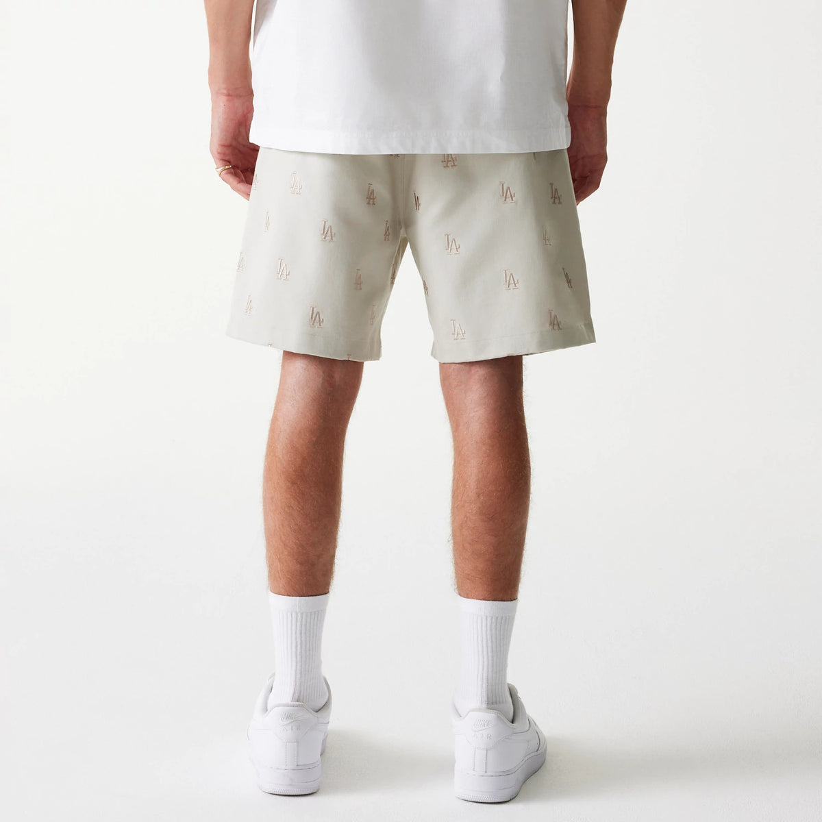 New Era LA Dodgers MLB Monogram Cream Shorts, on-model rear view showing cream shorts featuring an all-over monogram LA pattern, the hem resting above the knee, paired with white socks and trainers.