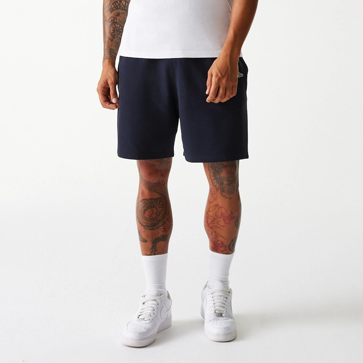 New Era New York Yankees MLB Pique Navy Shorts, front view showing the dark navy colour with a small raised New Era logo on the left leg near the hem, paired with a white T-shirt and white trainers.
