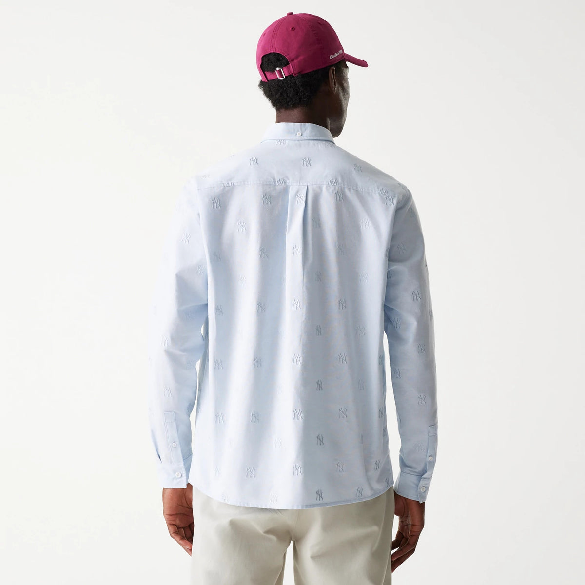 New Era New York Yankees MLB Monogram Pastel Blue Long Sleeve Shirt, rear view on a model wearing a red cap, showing the embroidered NY monogram pattern across the light blue fabric and buttoned cuffs.