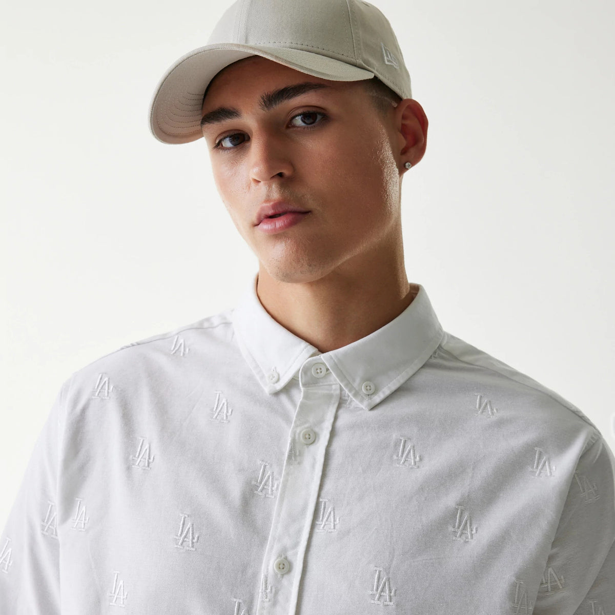 New Era LA Dodgers MLB Monogram White Long Sleeve Shirt, on-model showing the white embroidered LA logos evenly spaced across the shirt, styled with a beige cap featuring the New Era flag logo on the left side.