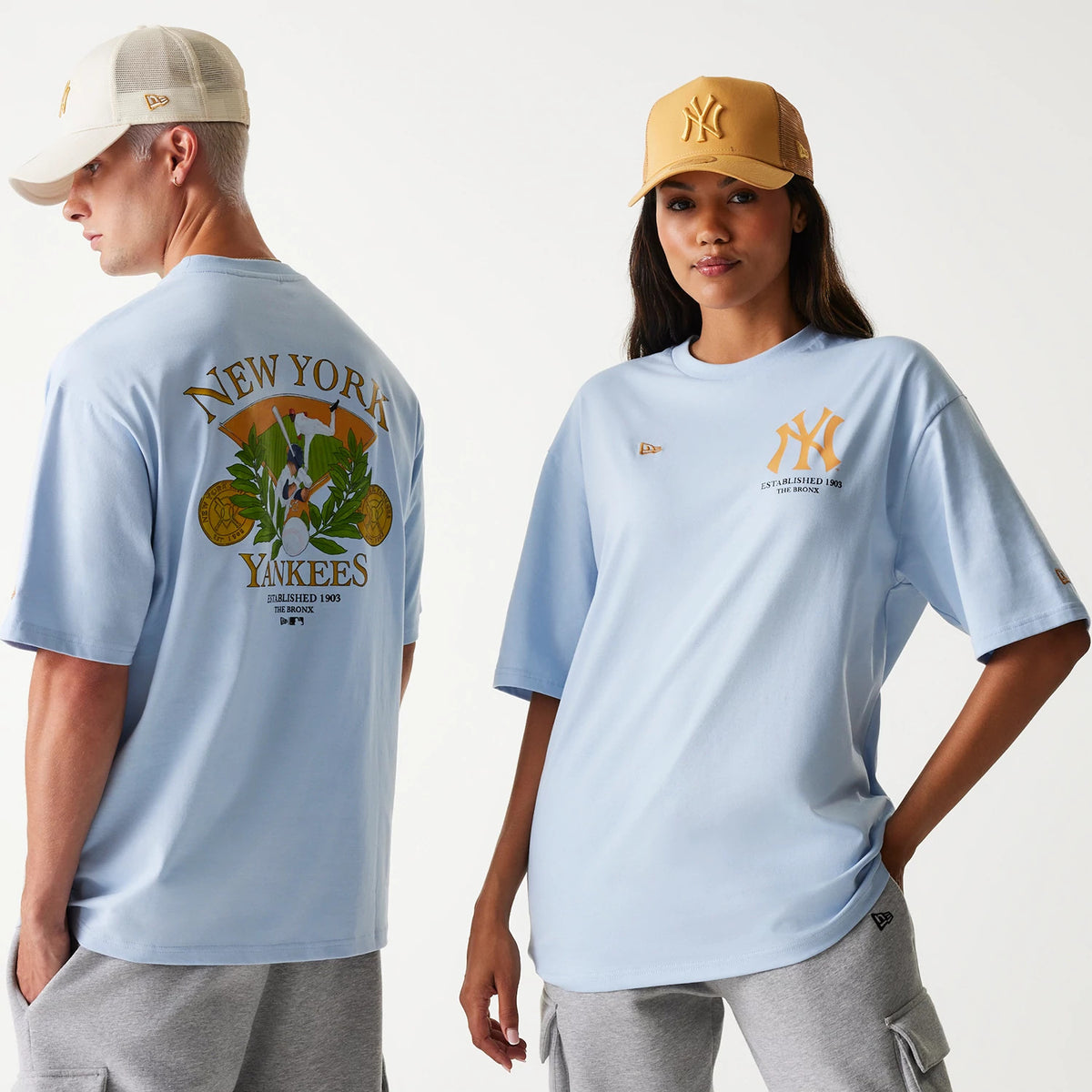 New Era New York Yankees MLB Baseball Graphic Pastel Blue Oversized T-Shirt, front and back view showing large graphic design on the back, team logo on the front, worn by a model in light grey shorts, with an embossed New Era logo on a beige cap.