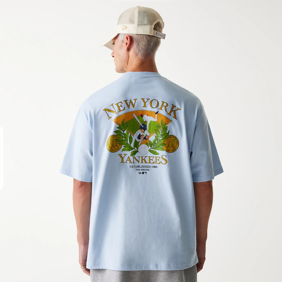 New Era New York Yankees MLB Baseball Graphic Pastel Blue Oversized T-Shirt, back view showing a large graphic with a baseball player, laurel leaves, baseballs, and text reading New York Yankees across the upper back.