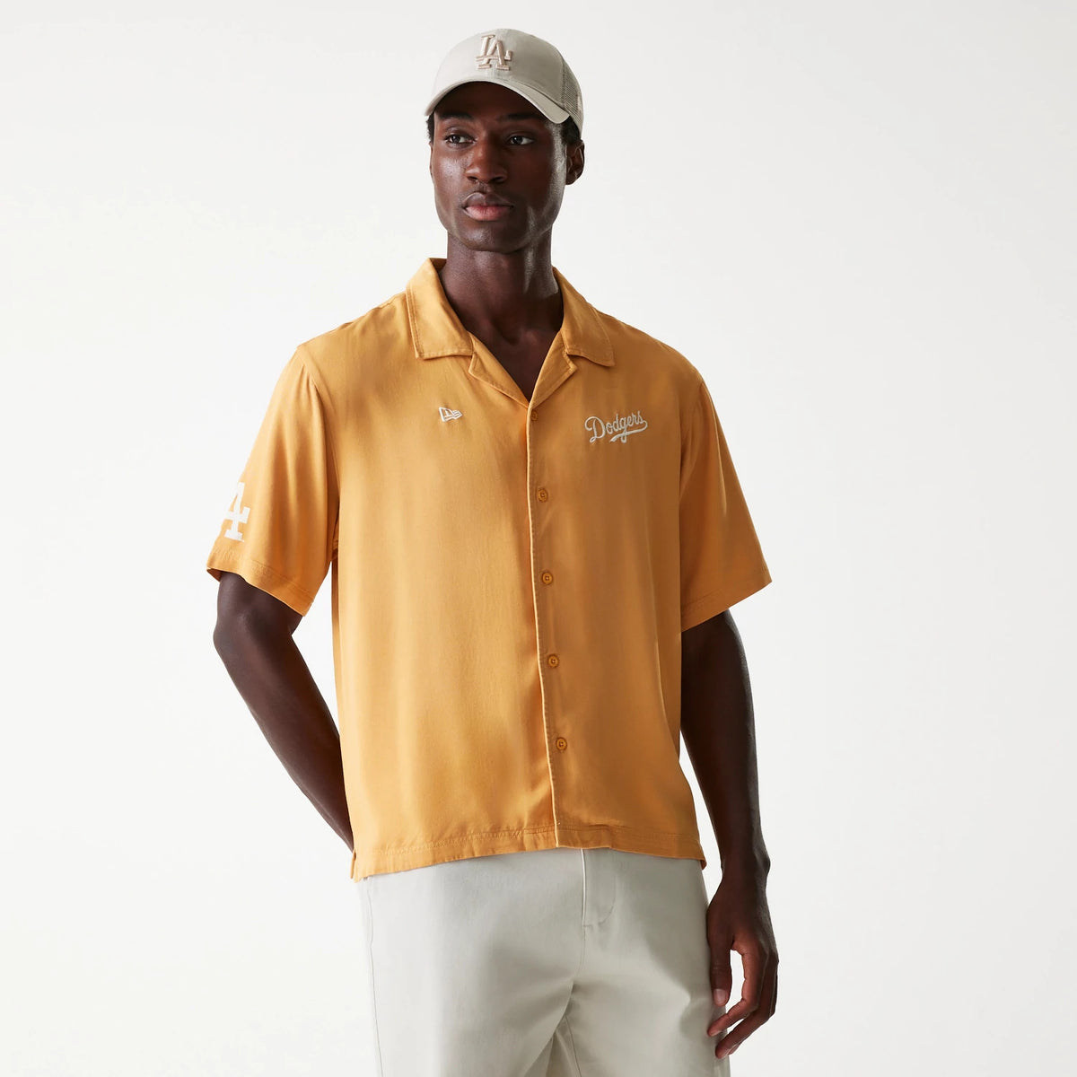 New Era LA Dodgers MLB Graphic Beige Revere Short Sleeve Shirt, front view on a model wearing a beige cap, featuring an embroidered Dodgers script on the chest and the LA logo on the right sleeve, with a New Era flag logo above the left chest pocket.