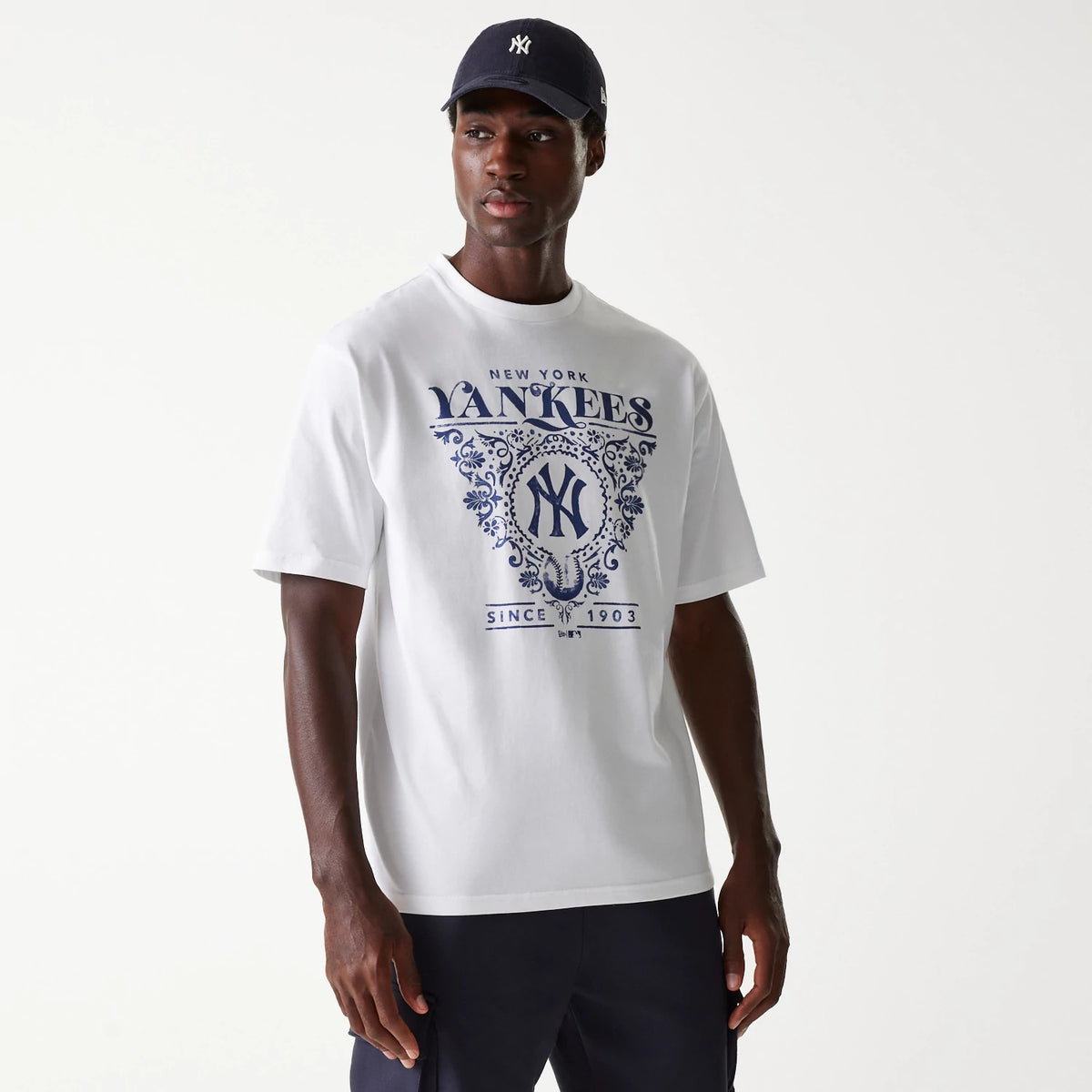 New Era New York Yankees MLB Floral Graphic White Oversized T-Shirt, on-model view showing a large blue floral graphic with the Yankees logo centred on the chest, paired with a navy cap featuring the New Era logo on the side.