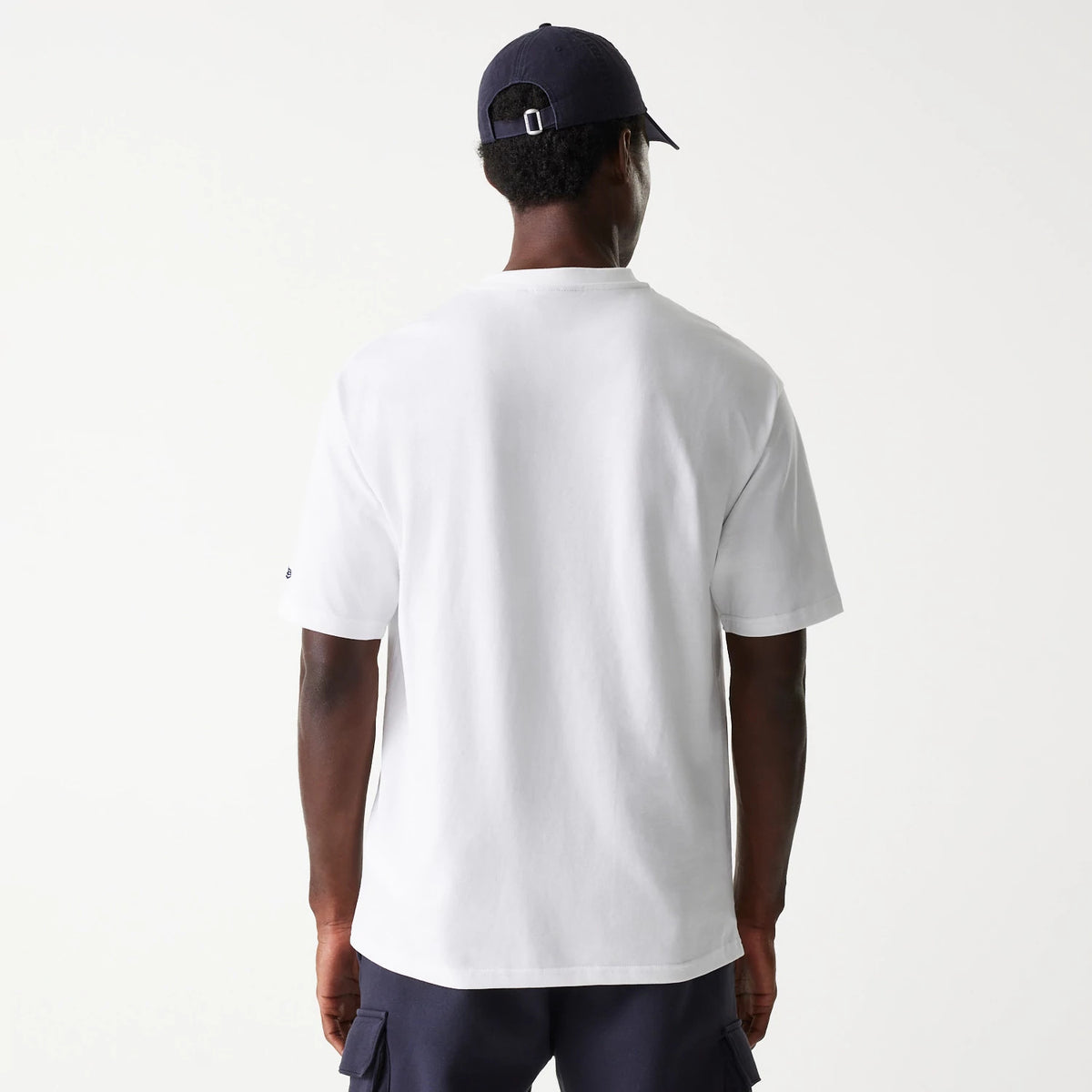 New Era New York Yankees MLB Floral Graphic White Oversized T-Shirt, rear view showing plain white fabric on the back of the shirt, short sleeves and a small debossed New Era logo on the left sleeve, worn by a person also in a dark cap.